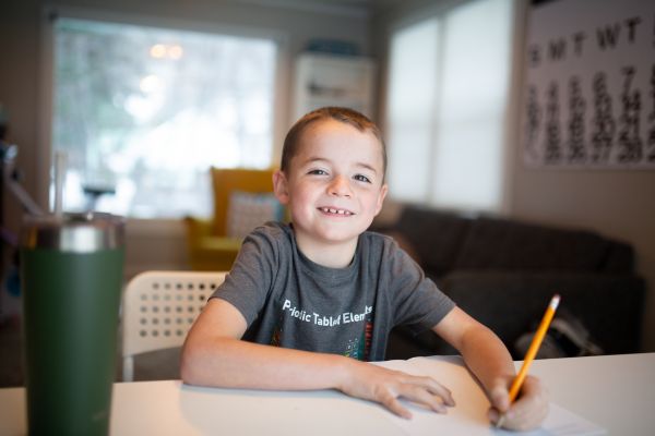 Junge sitzt am Küchentisch und macht Hausaufgaben – Symbol für den Alltag, den der Elternabend Hausaufgaben und selbständiges Lernen mit Andrea Hüppin aufgreift