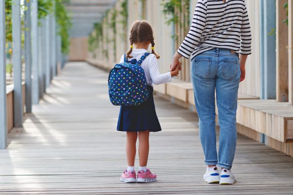 Mädchen mit Schulrucksack hält die Hand der Mutter – symbolisiert Vorbereitung auf den Schulstart